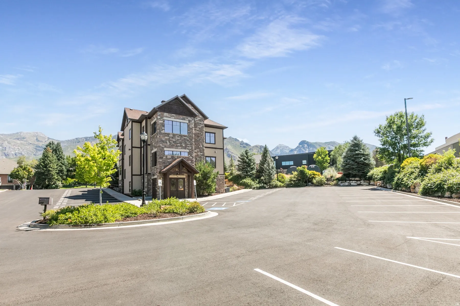 Stone and siding exterior with a prominent entrance, surrounded by landscaped grounds and mountains in the distance
