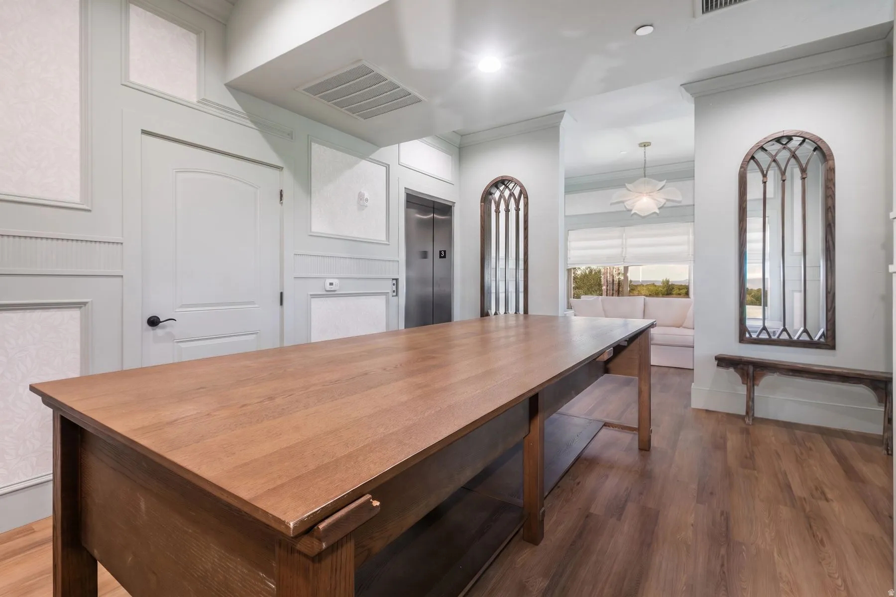 Wood-finish flooring, accent wall paneling, stainless steel elevator, and decorative arched mirrors
