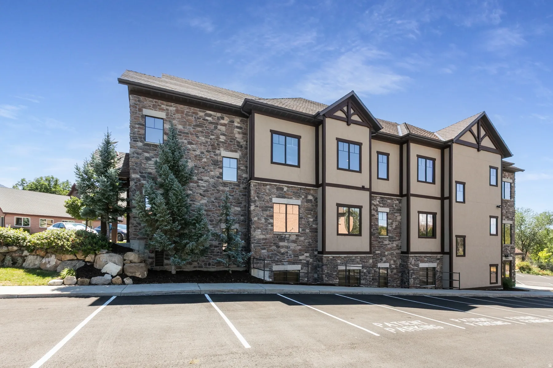 Stone and stucco exterior with multiple gables, framed windows, and a paved parking area