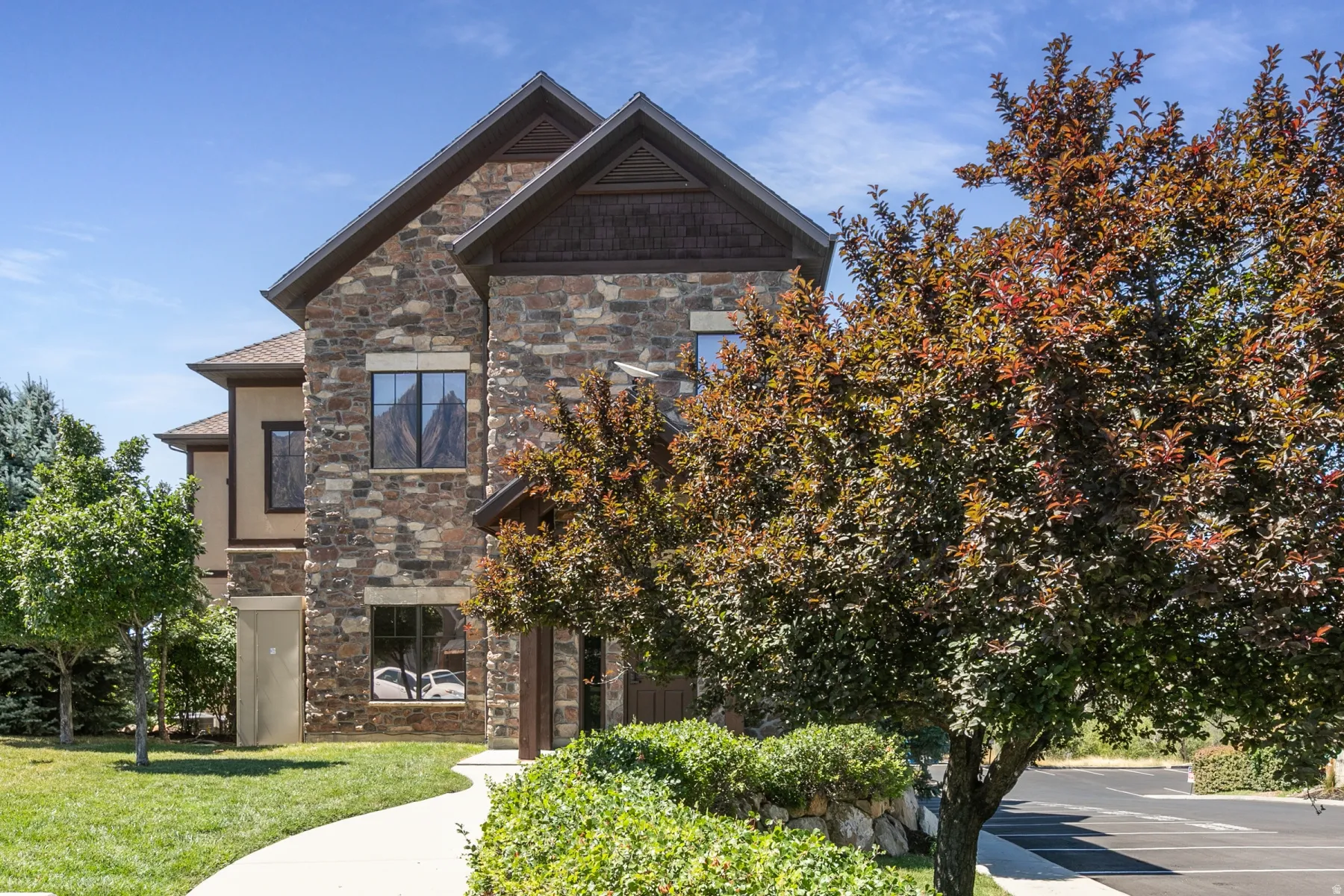 Stone and stucco exterior with multiple gables, dark trim, and a concrete pathway