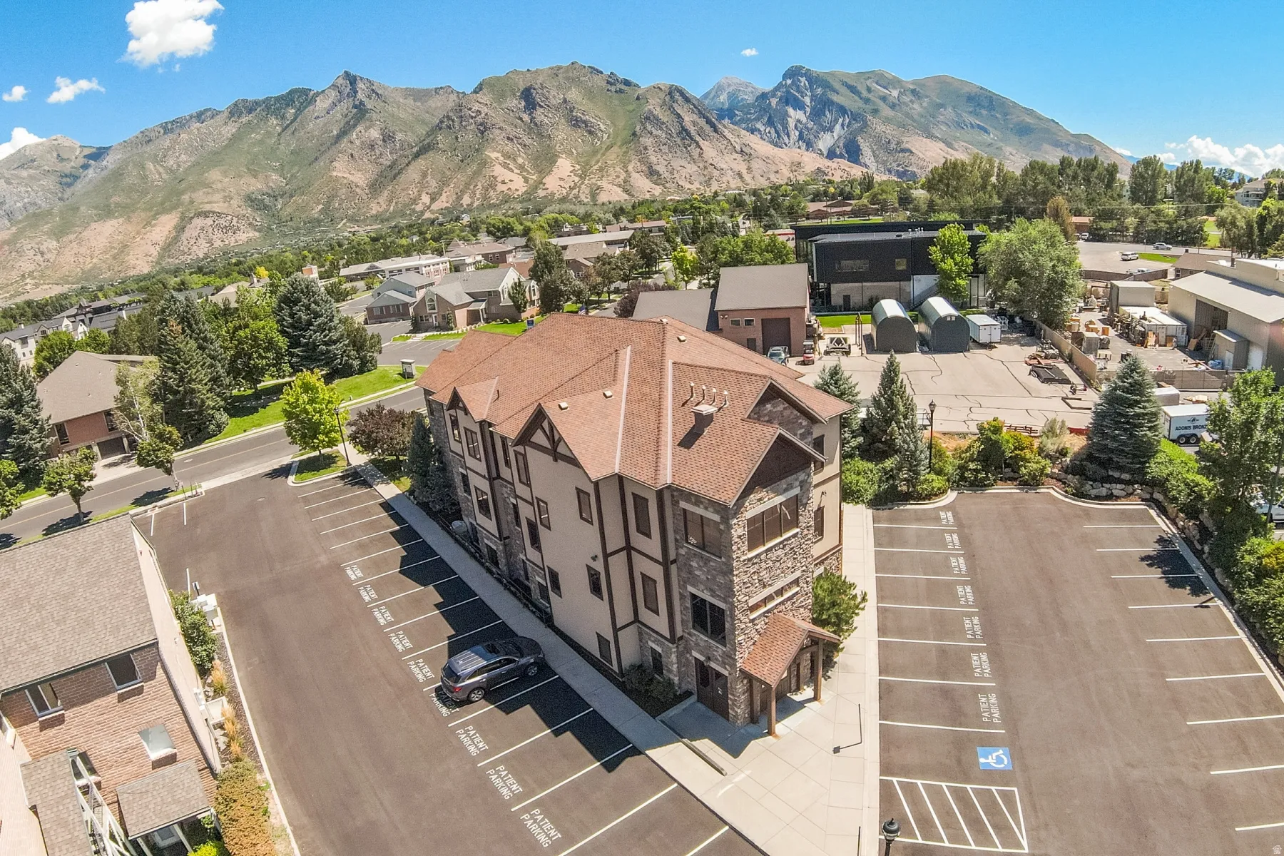 Multi-story commercial building featuring stone and stucco facade, an asphalt parking lot with marked spaces, and a prominent mountain backdrop