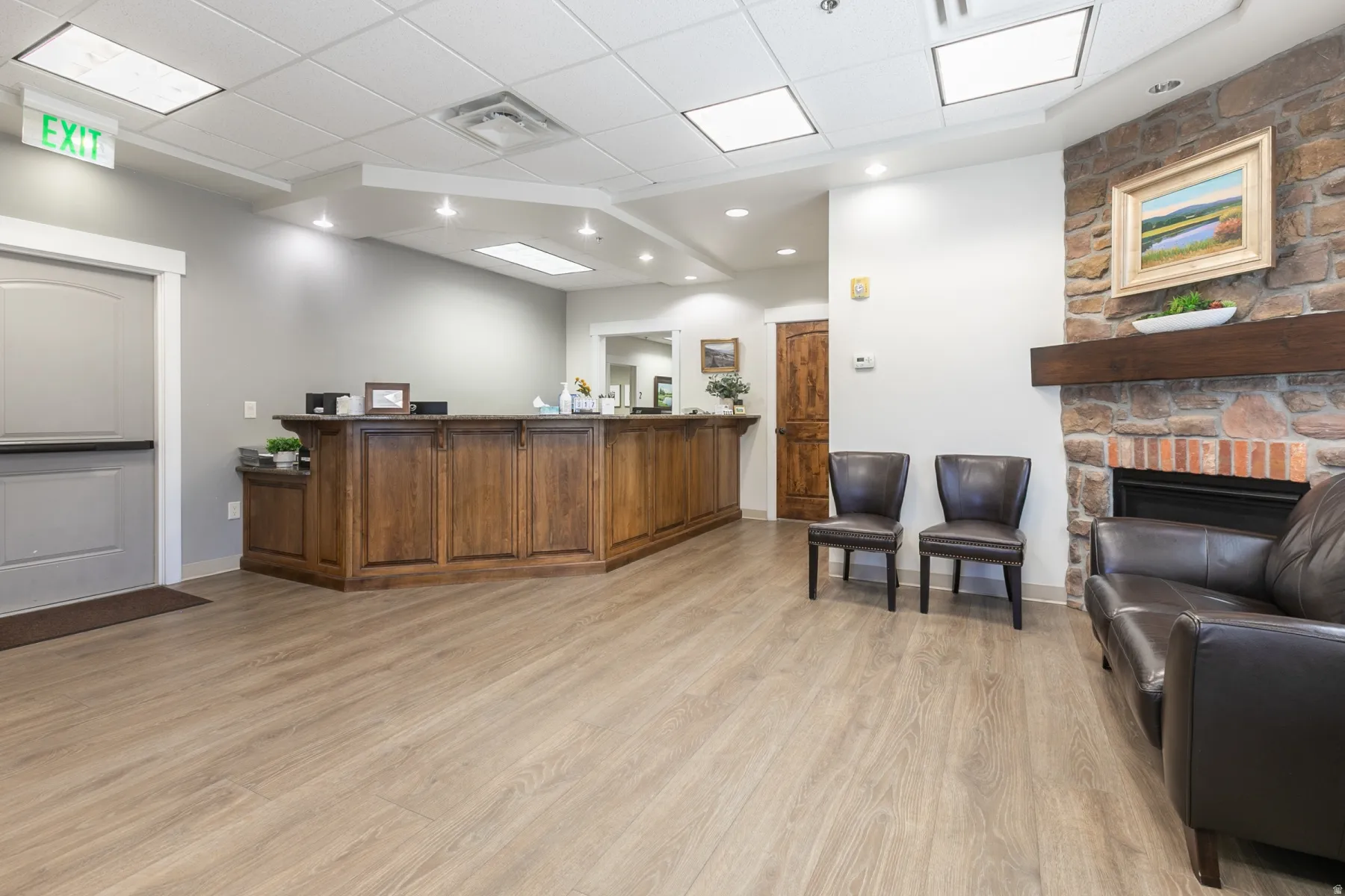 Wood-finish flooring throughout, stone-clad fireplace with wood mantel, built-in reception desk with wood-finish cabinetry, recessed lighting, and a drop ceiling