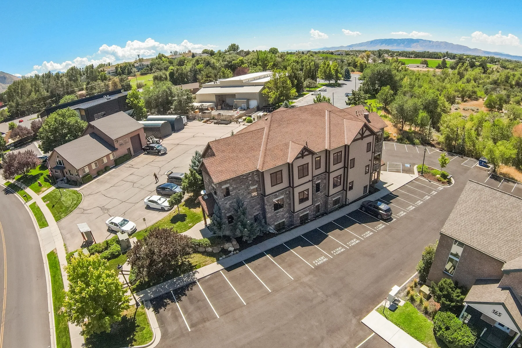 Stone and stucco exterior with multiple gables, extensive paved parking, and mature landscaping