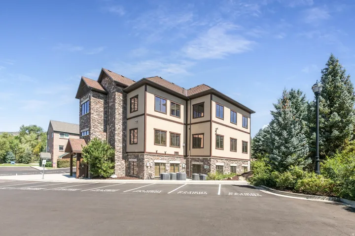 Stone and stucco exterior, multi-story structure, ample paved parking, mature evergreen landscaping, and a covered entry