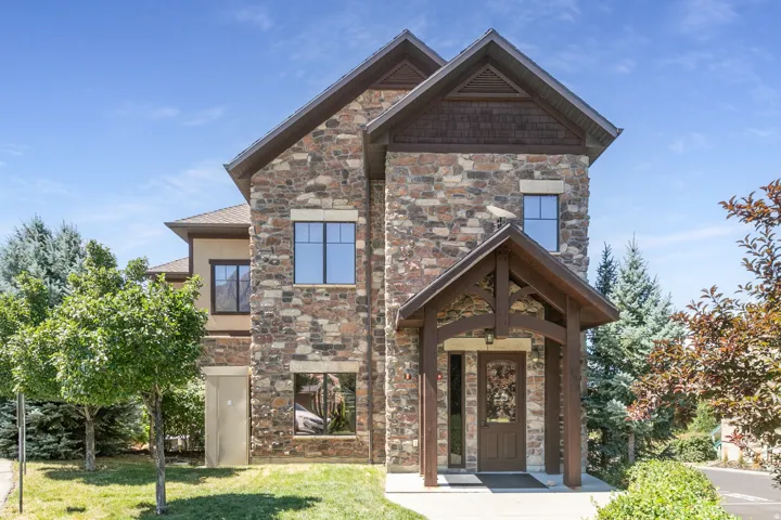 Stone and stucco exterior with multiple windows, featuring a prominent covered entry with exposed wood beams and a wood-paneled door