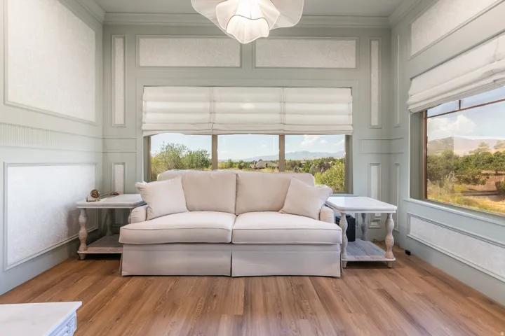 Wood-finish flooring, paneled walls with textured inserts, large windows, and custom window treatments