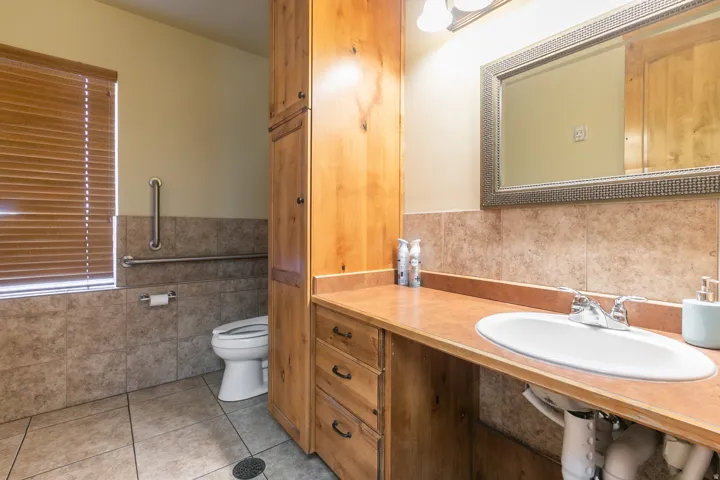 Tile flooring, wood-finish vanity with an integrated sink, built-in storage cabinet, framed mirror, and chrome fixtures