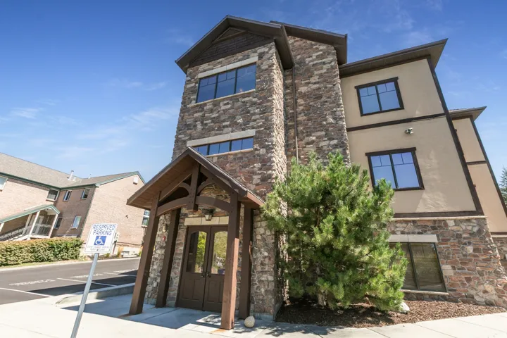 Exterior featuring stone and stucco facade, wood-finish gabled entry, dark-framed windows, and mature landscaping
