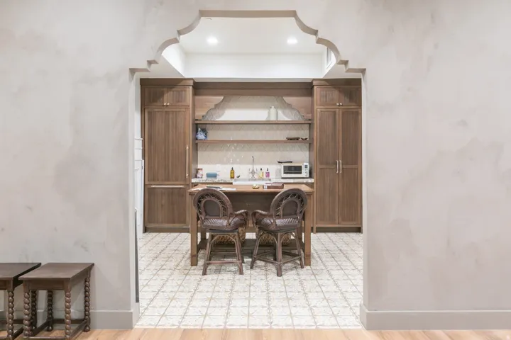 Archway entry with decorative detailing, custom wood cabinetry, integrated refrigerator, geometric tile flooring, and open shelving