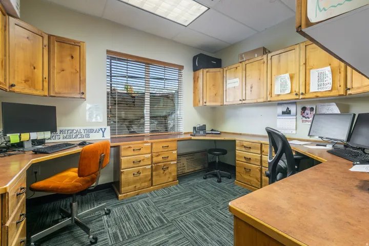 Expansive office space featuring wood-finish cabinetry, built-in desks, and patterned carpet flooring