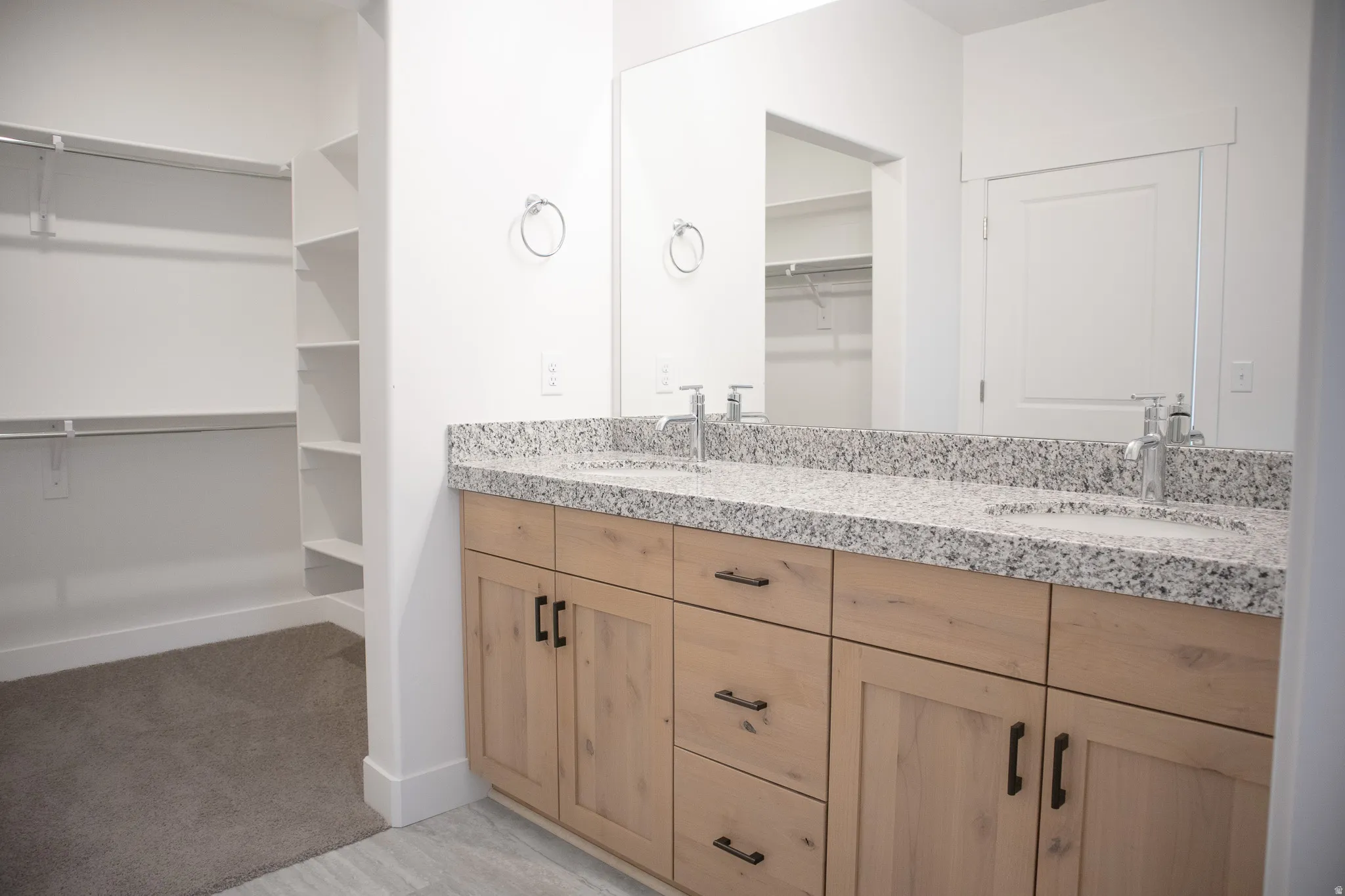 Primary bath with dual sinks, stained wood cabinets and granite slab countertops.
