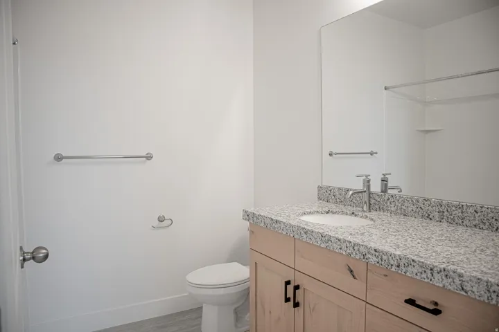 Full secondary bath with stained wood cabinets and granite slab countertops.