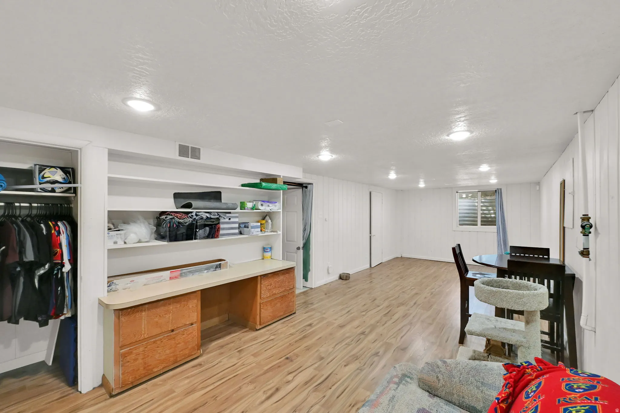 Recessed ceiling lighting, wood-finish flooring, built-in shelving, built-in desk with wood-finish cabinetry, and a full-size window