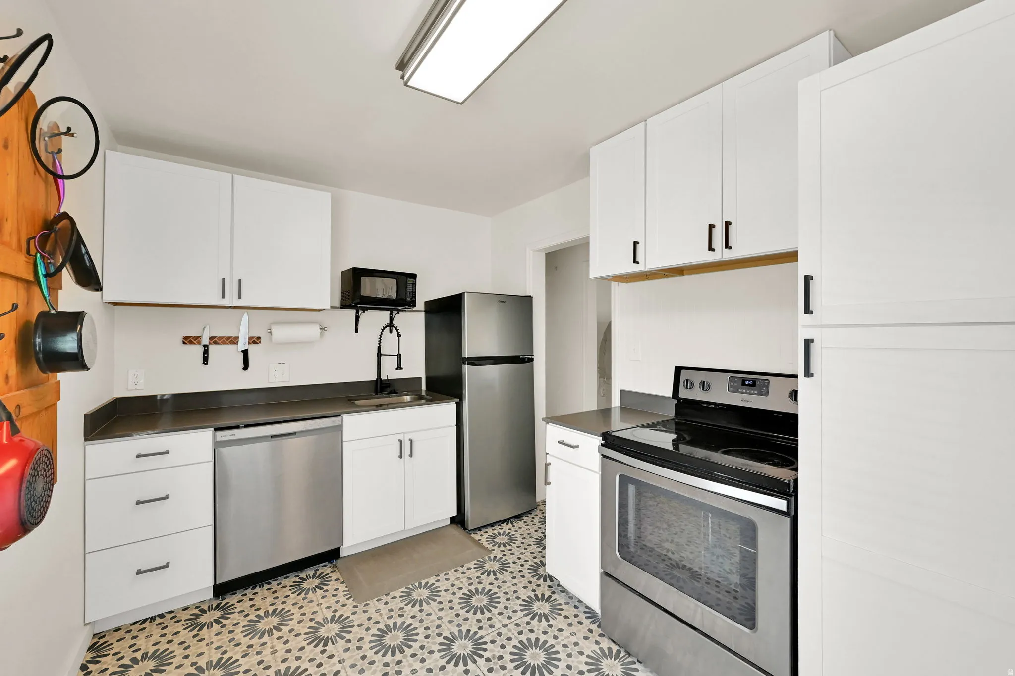 Contemporary kitchen featuring white cabinetry, stainless steel appliances, patterned floor tiling, and dark countertops