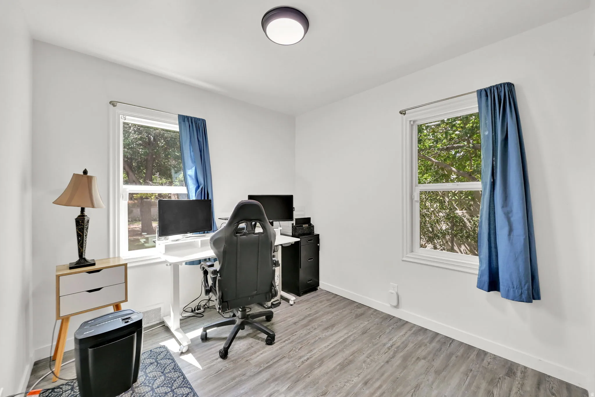 White interior walls, wood-finish flooring, two windows with natural light, and a ceiling-mounted light fixture