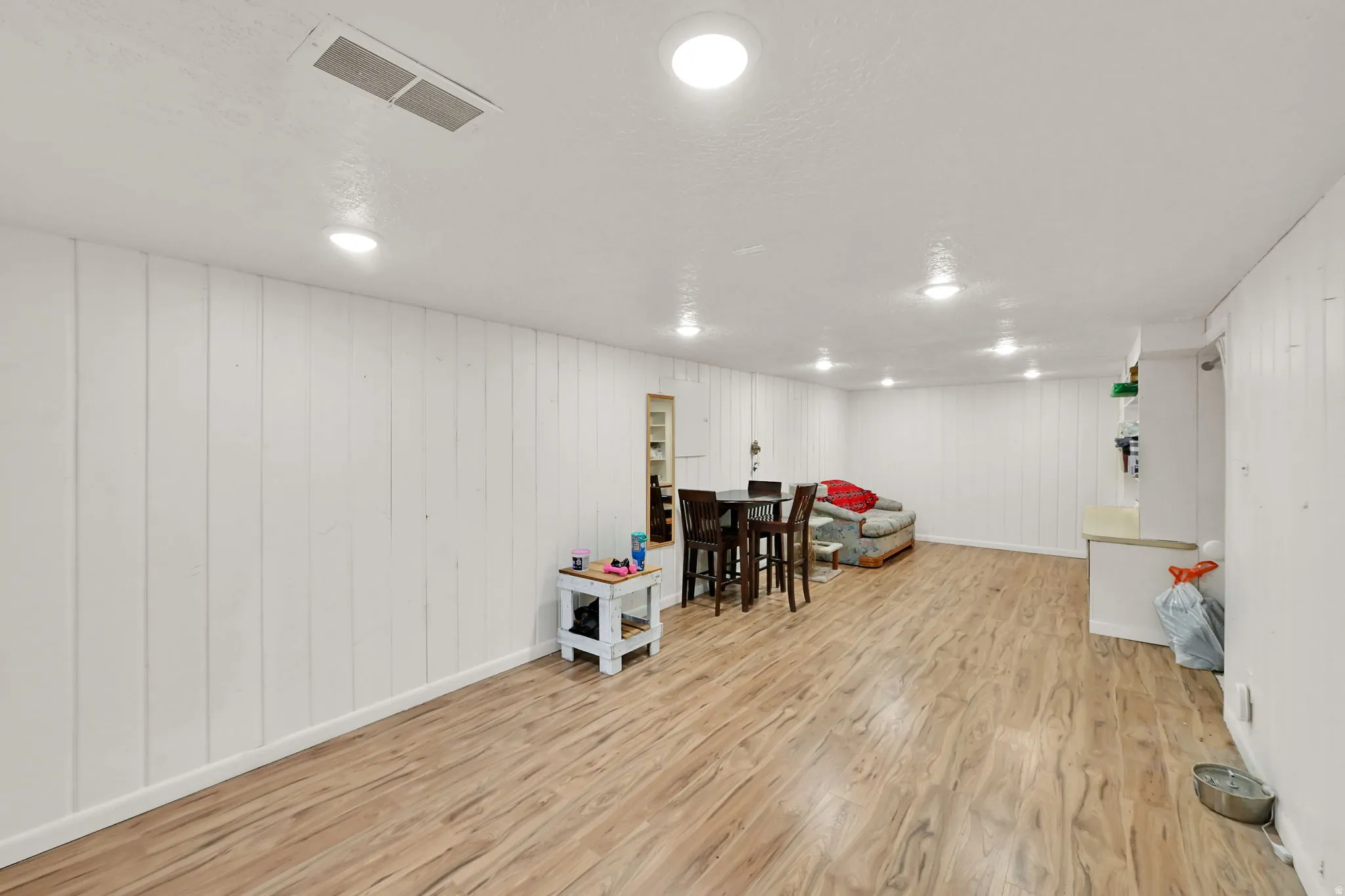 Recessed lighting illuminates wood-finish flooring and white plank walls