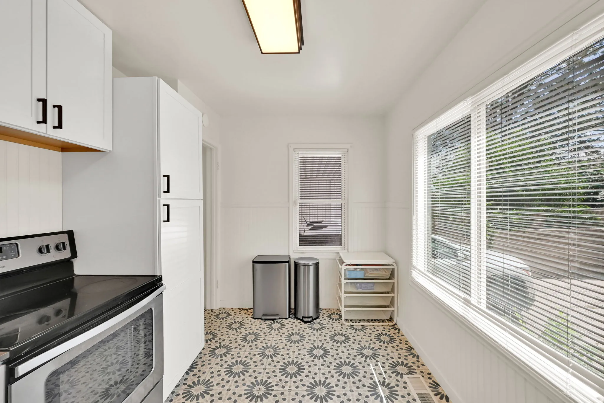 White cabinetry with matte black hardware, stainless steel range, patterned floor tiling, and a large window