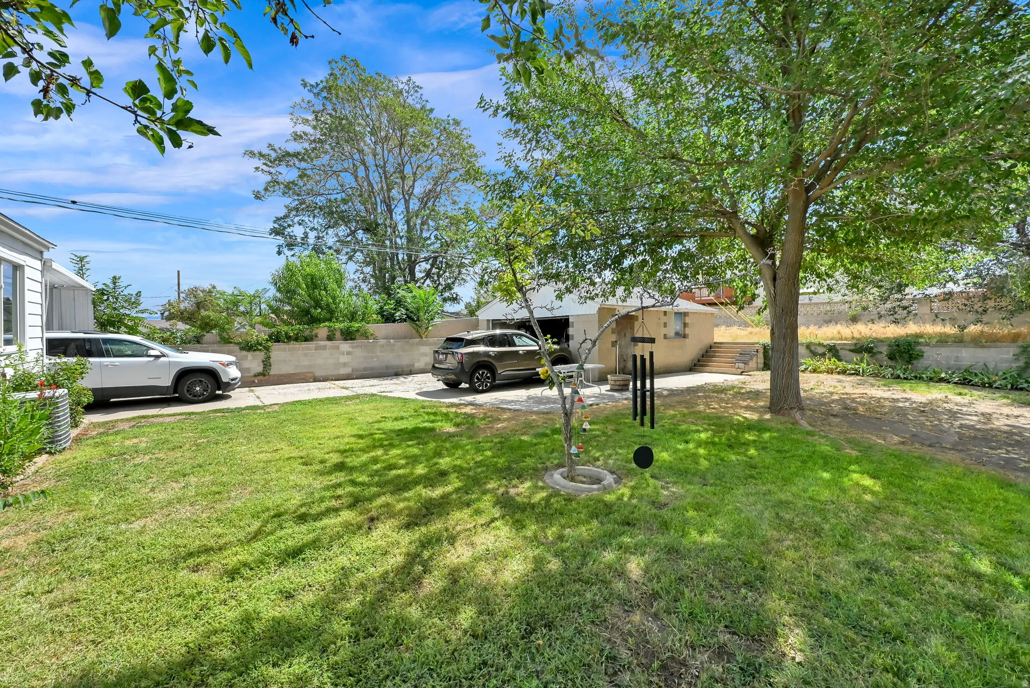 Expansive grassy yard with mature trees, offering a concrete driveway and privacy fencing