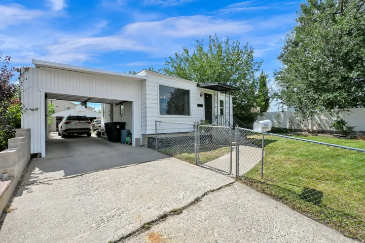 White siding exterior with a covered carport, concrete driveway, front entrance with an overhang, and a fenced front yard