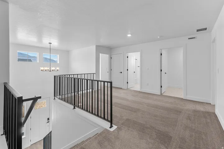 Upper-level landing with neutral carpeting, white walls, black metal railings, and a chandelier