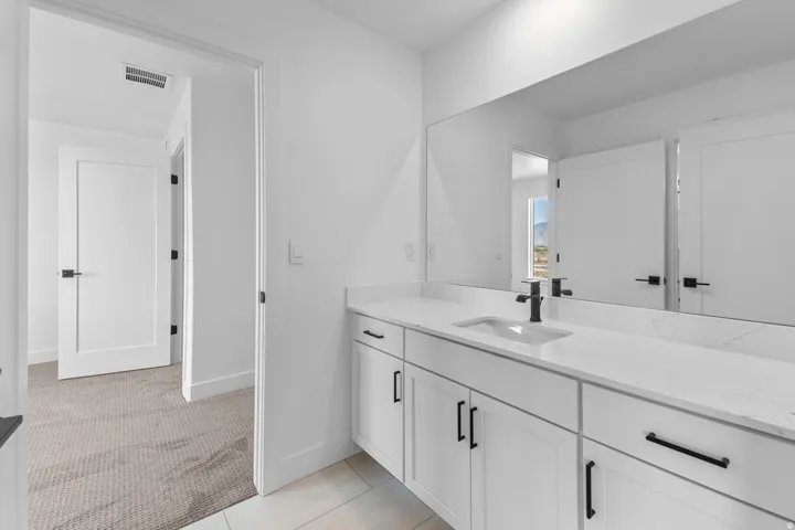 Double vanity with a white rectangular undermount sink, quartz countertop, black faucet, and white shaker-style cabinetry with black hardware