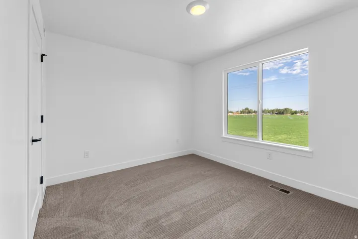 Neutral-toned carpet flooring, white walls, and a large window providing expansive green field scenery