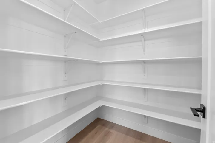 Expansive corner pantry featuring white shelving, multiple storage levels, wood-finish flooring, and a matte black door handle