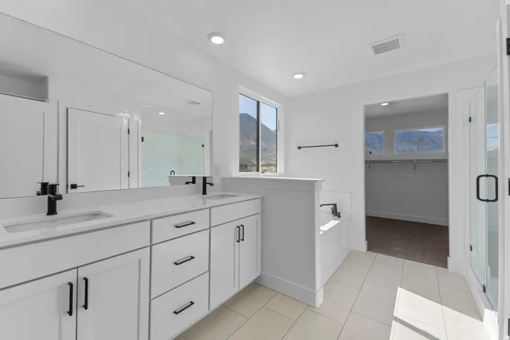 Dual vanity with white cabinetry, matte black hardware, and an expansive mirror