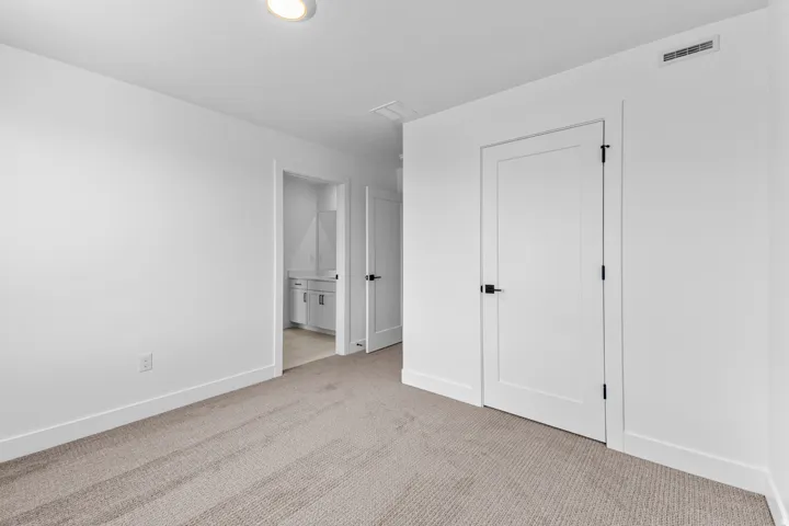 Neutral-toned carpeting, white interior doors with matte black hardware, recessed ceiling lighting, and a white vanity with a rectangular sink