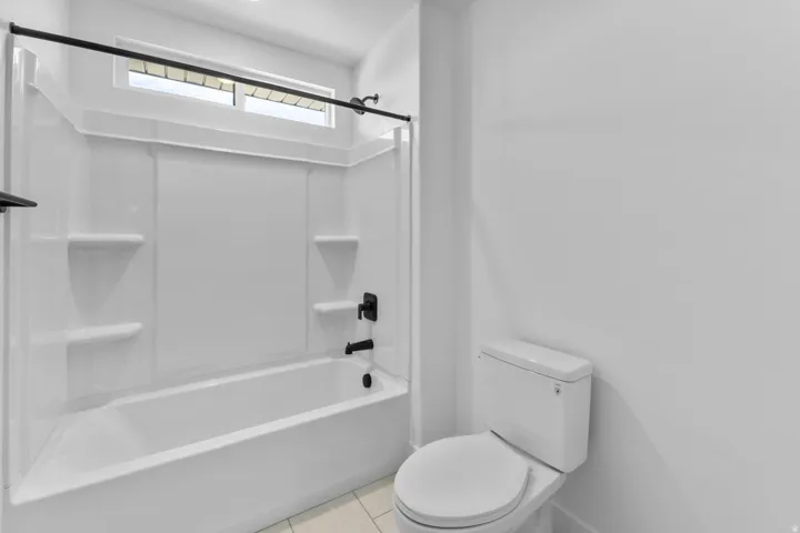 Bathtub with integrated shelving, matte black fixtures, and an overhead window