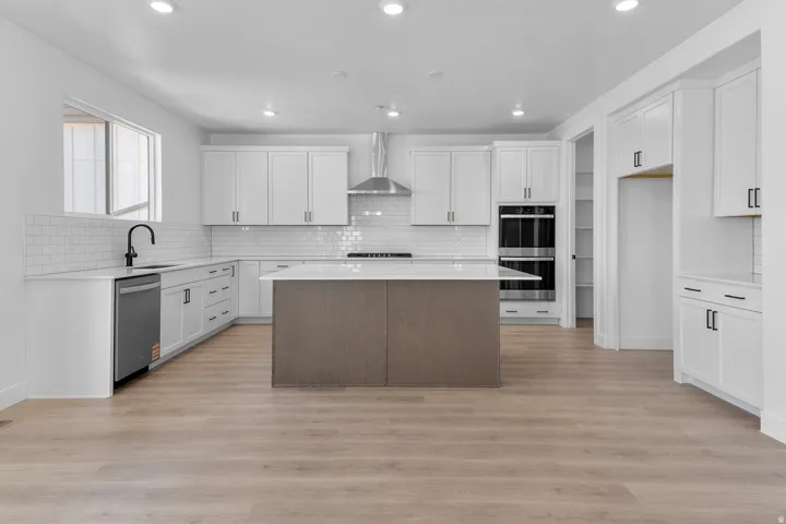 Spacious kitchen featuring white cabinetry, a center island with countertop, stainless steel appliances, and wood-finish flooring