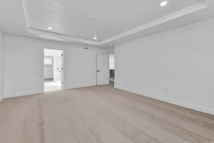 Recessed lighting, tray ceiling, neutral carpet flooring, white interior doors, and black door hardware