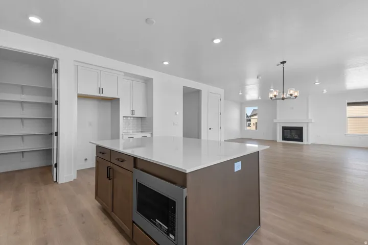 Kitchen island with integrated microwave and white countertop, white shaker cabinetry with subway tile backsplash, recessed lighting, and wood-finish flooring