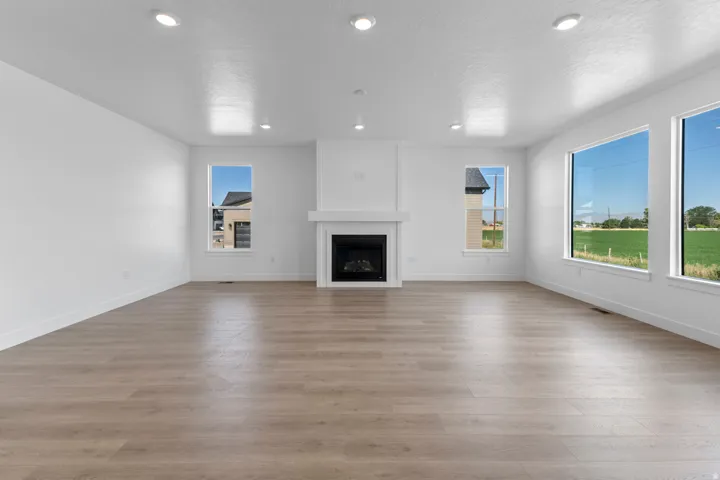 Open-concept living space with wood-finish flooring, a central fireplace, multiple windows, and recessed ceiling lighting