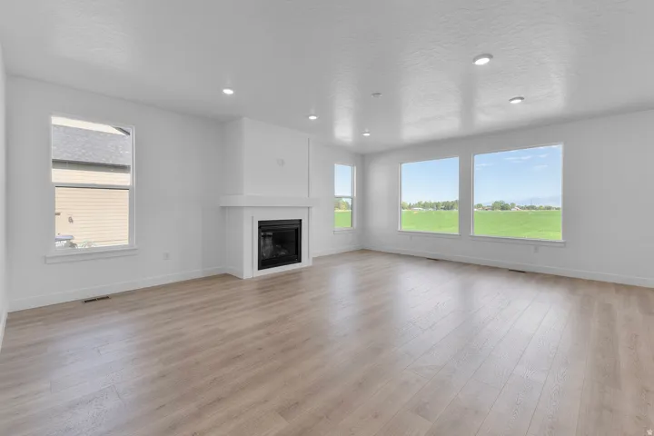 Spacious living area featuring wood-finish flooring, a contemporary fireplace, multiple windows with expansive outdoor scenery, and recessed lighting