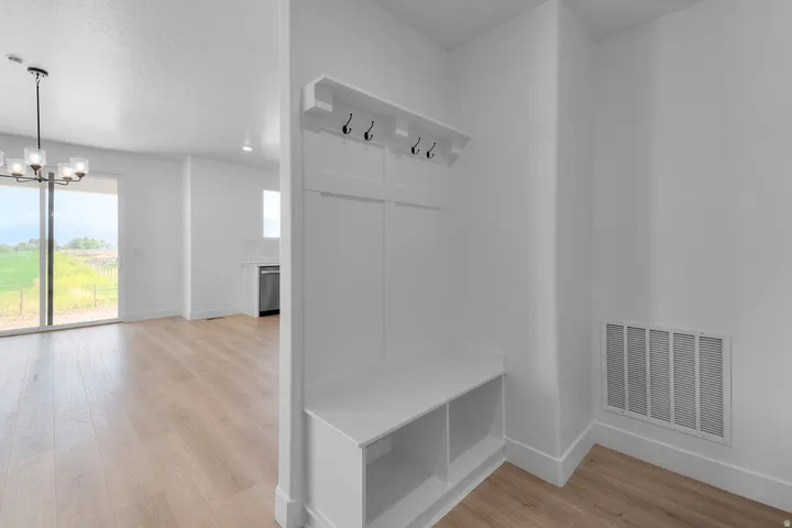 Built-in bench with storage and coat hooks, wood-finish flooring, sliding glass door, white subway tile backsplash, and stainless steel dishwasher