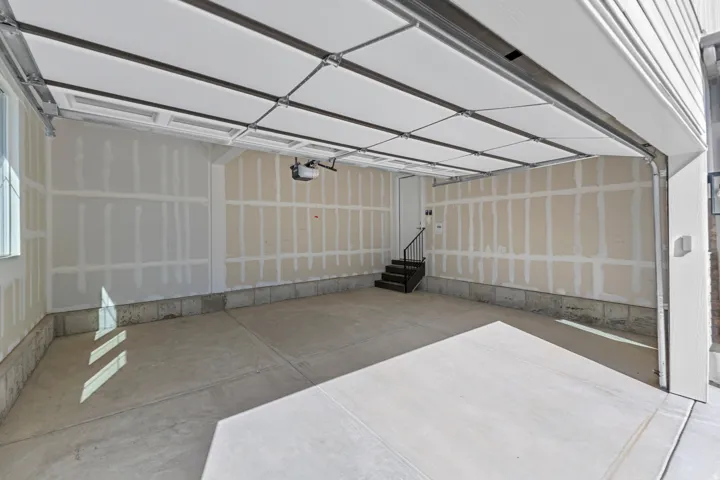 Concrete flooring in garage featuring a white overhead door and an interior staircase with metal railing