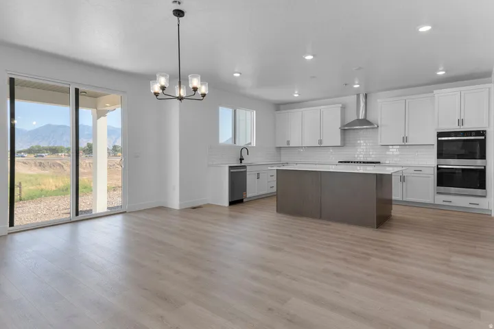 Open concept kitchen and living space featuring wood-finish flooring, white shaker cabinetry, a central island with a solid surface countertop, and double wall ovens