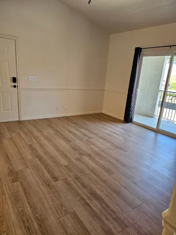 Vaulted ceiling, wood-finish flooring, wainscoting, sliding glass door, and exterior balcony with metal railing
