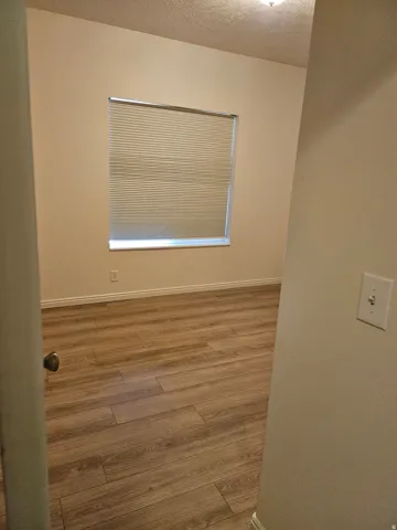 Wood-finish flooring, neutral wall tones, window with horizontal blinds, and a ceiling-mounted light fixture