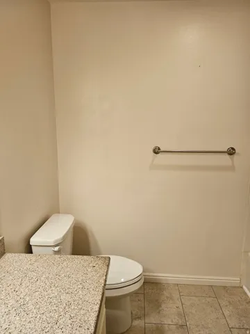 White toilet with a round bowl, granite-finish countertop, and tile flooring