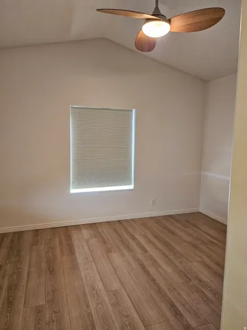 Wood-finish flooring with a ceiling fan and a window featuring horizontal blinds