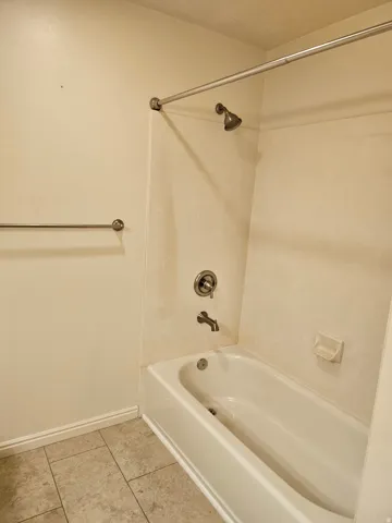 Bathtub with shower fixture, a chrome towel bar, and tiled flooring