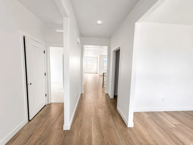 Expansive hallway featuring wood-finish flooring, white walls, recessed ceiling lighting, and white doors