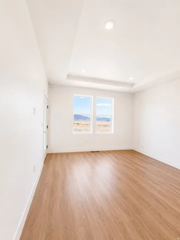 Recessed lighting, tray ceiling, two windows, wood-finish flooring, and white walls