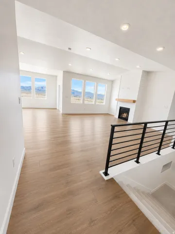 Spacious room with wood-finish flooring, a contemporary fireplace, multiple large windows, recessed ceiling lights, and a modern black horizontal railing