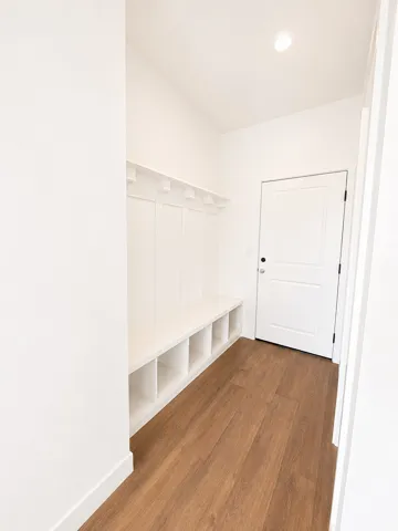 Bright mudroom featuring built-in cubbies with generous storage, warm wood-finish flooring, recessed ceiling lighting, and white shaker-style door with hardware