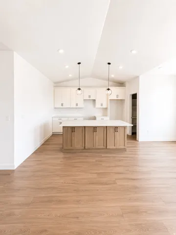 Vaulted ceiling with recessed lighting, wood-finish flooring, two-tone cabinetry, central island with light-toned countertop, and pendant lighting