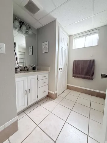 Bathroom featuring a vanity with white cabinetry, a rectangular mirror, a window with blinds, and light-toned floor tiling