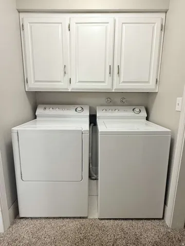 Laundry area featuring white cabinetry with brushed nickel hardware, light neutral wall paint, and carpet flooring